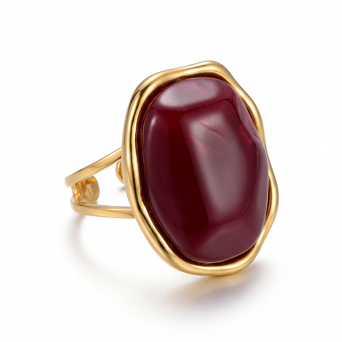 Bague dorée sertie d'un gros cabochon bordeaux brillant, sur fond blanc