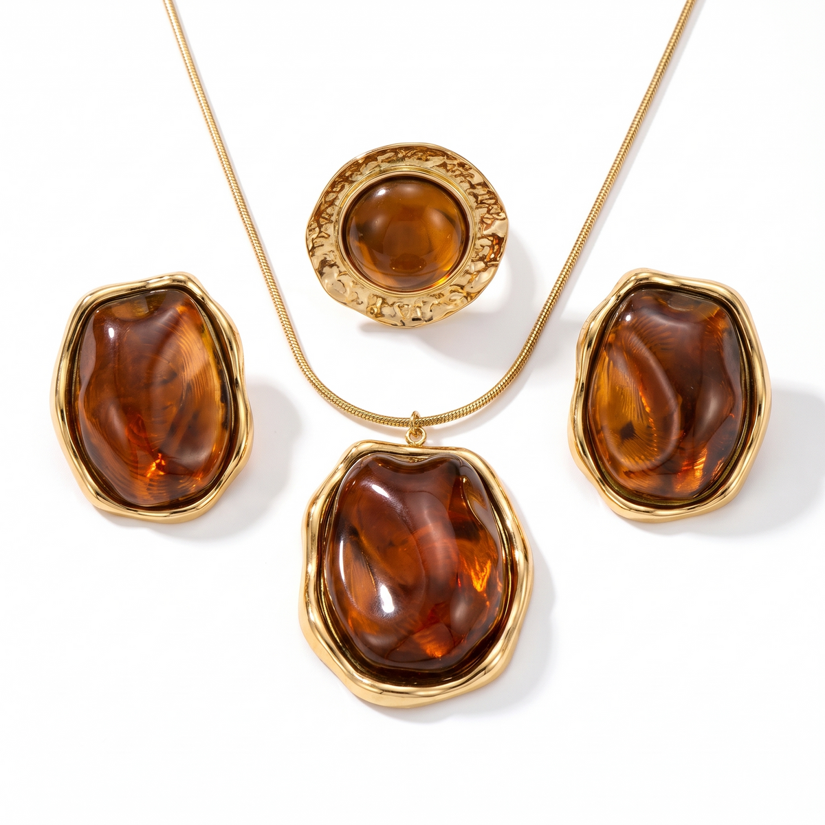 Parure dorée avec collier chaîne serpent, boucles d'oreilles et bague à cabochon couleur ambre, sur fond blanc