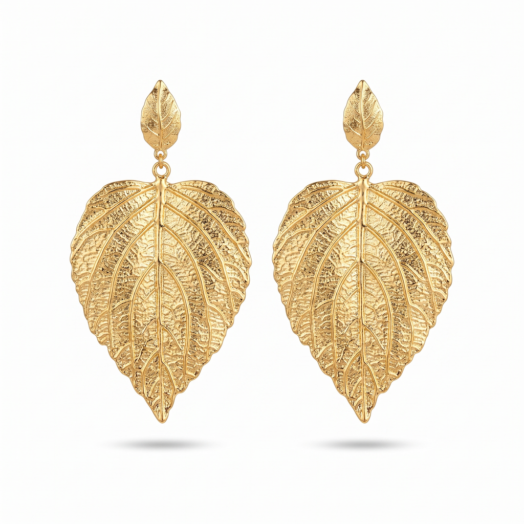Paire de grandes boucles d'oreilles en forme de feuille dorée aux nervures en relief, sur fond blanc