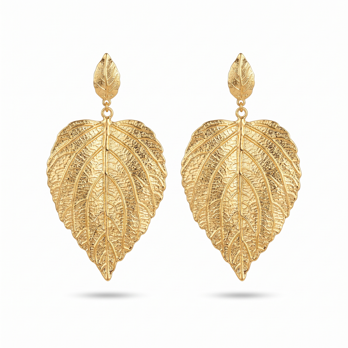 Paire de grandes boucles d'oreilles en forme de feuille dorée aux nervures en relief, sur fond blanc