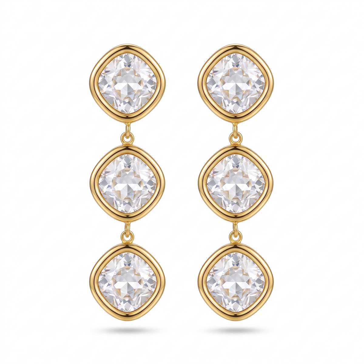 Paire de boucles d'oreilles pendantes dorées à trois cristaux taille coussin en cascade, sur fond blanc