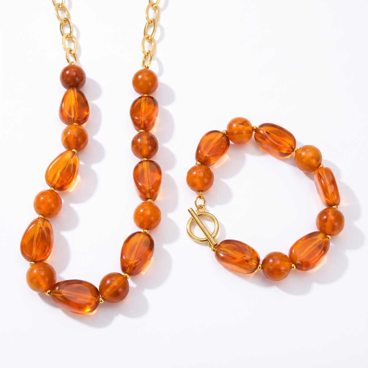 Parure collier et bracelet de perles en résine couleur ambre et chaînes dorées, fermoirs à bascule, sur fond blanc